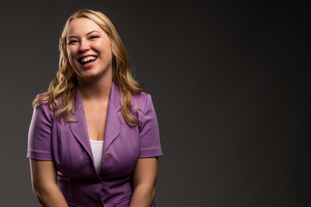 Picture of a girl smiling in a purple shirt in front of a black background